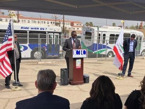 Man speaking at podium in front of bus. 